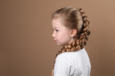 Photo of Little girl with braided hair on light brown background. Space for text