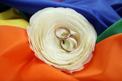 Photo of Wedding rings and flower on rainbow LGBT flag, closeup