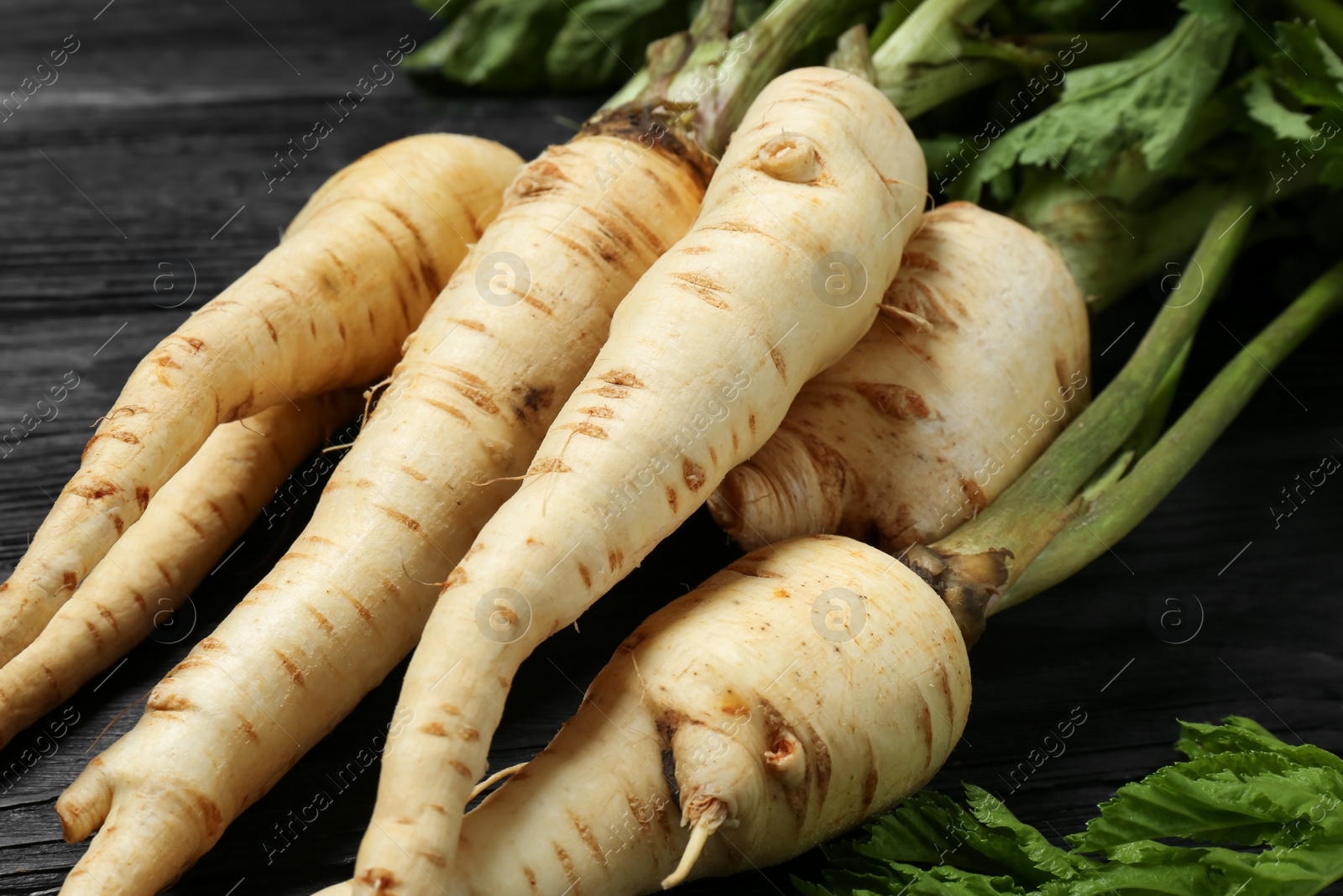 Photo of Tasty fresh ripe parsnips on black wooden table, closeup