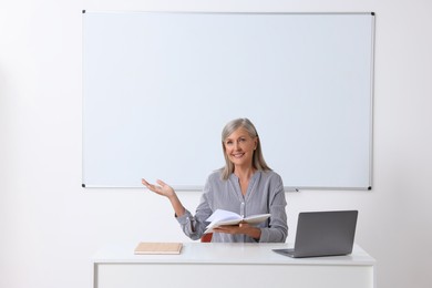 Happy professor giving lecture near laptop at desk in classroom, space for text