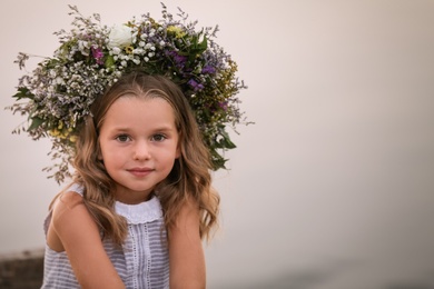 Photo of Cute little girl wearing wreath made of beautiful flowers on blurred background