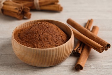 Aromatic cinnamon powder in bowl and sticks on white wooden table, closeup