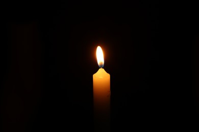 Photo of One burning wax candle on black background