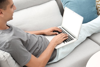 Photo of Man in casual clothes using laptop on sofa at home