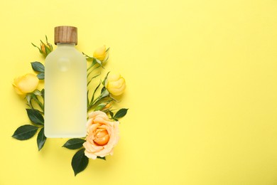 Bottle of rose essential oil and beautiful flowers on pale yellow background, top view. Space for text