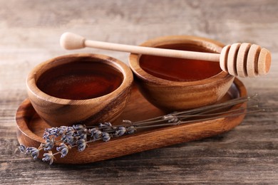 Photo of Delicious honey in bowls, lavender flowers and dipper on wooden table
