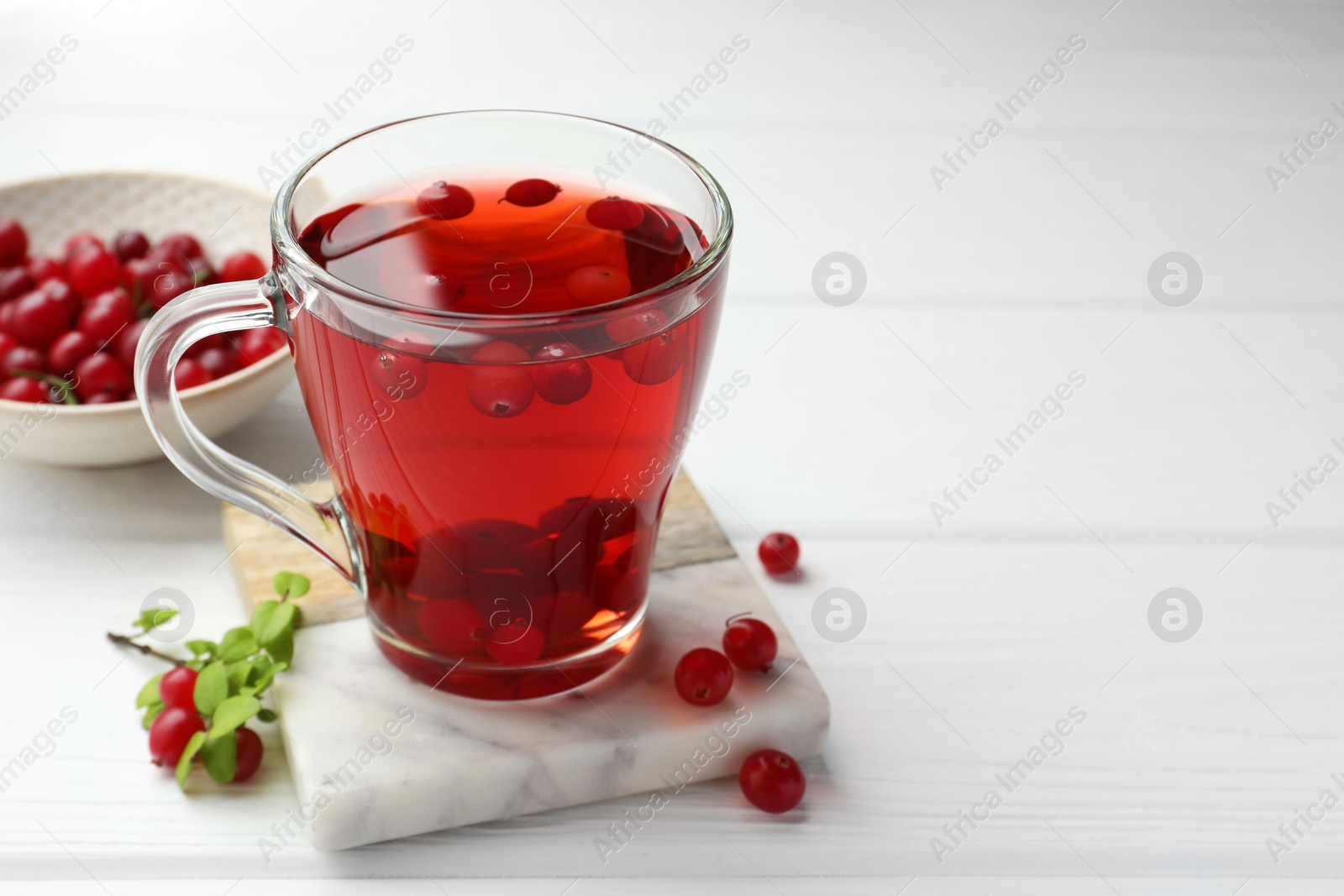 Photo of Tasty hot cranberry tea in glass cup and fresh berries on white wooden table