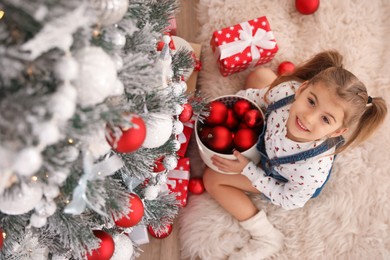 Photo of Cute little girl decorating Christmas tree at home, above view