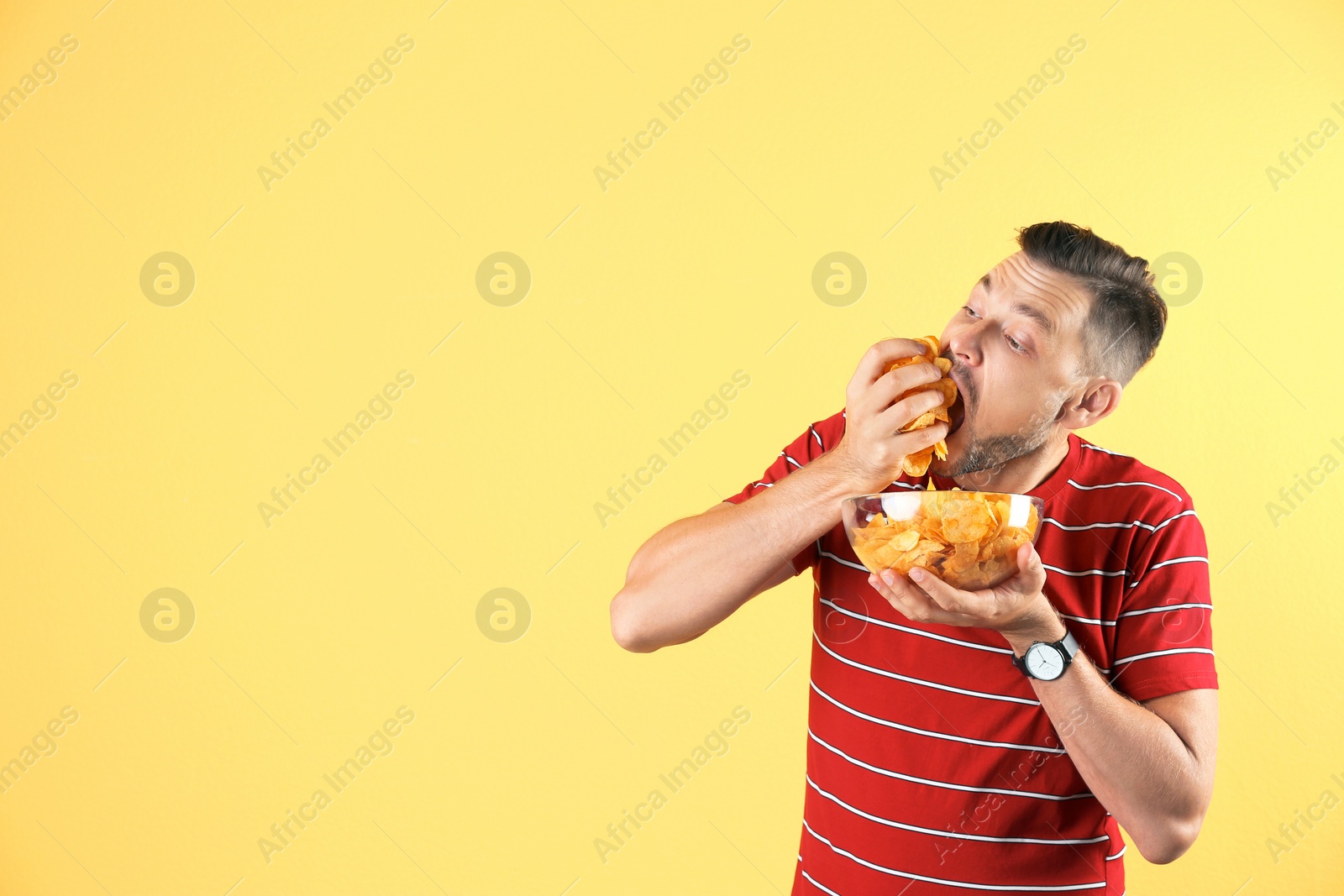 Photo of Man eating potato chips on color background. Space for text