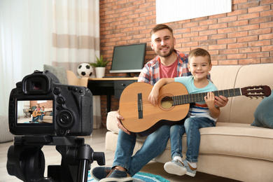 Image of Father and son recording guitar lesson indoors. Teaching music