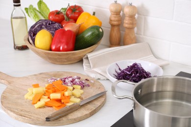 Board with cut vegetables and knife on white countertop in kitchen