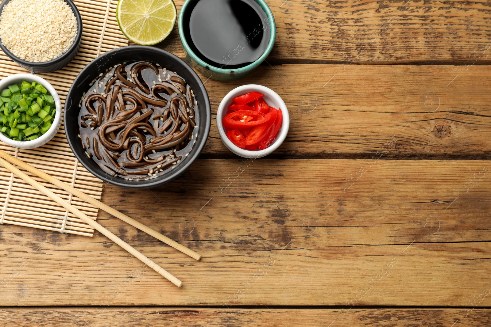 Photo of Tasty soup with buckwheat noodles (soba) and chopsticks served on wooden table, flat lay. Space for text