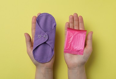 Photo of Woman holding disposable and reusable cloth menstrual pads on yellow background, top view
