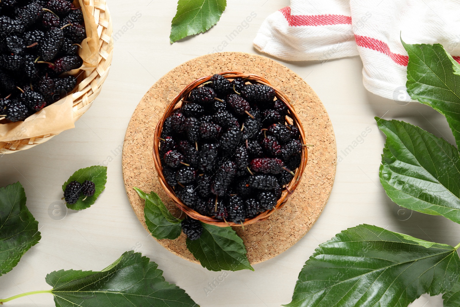 Photo of Wicker basket of delicious ripe black mulberries on white table, flat lay