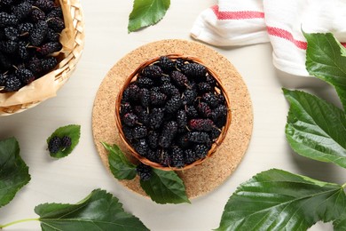 Wicker basket of delicious ripe black mulberries on white table, flat lay