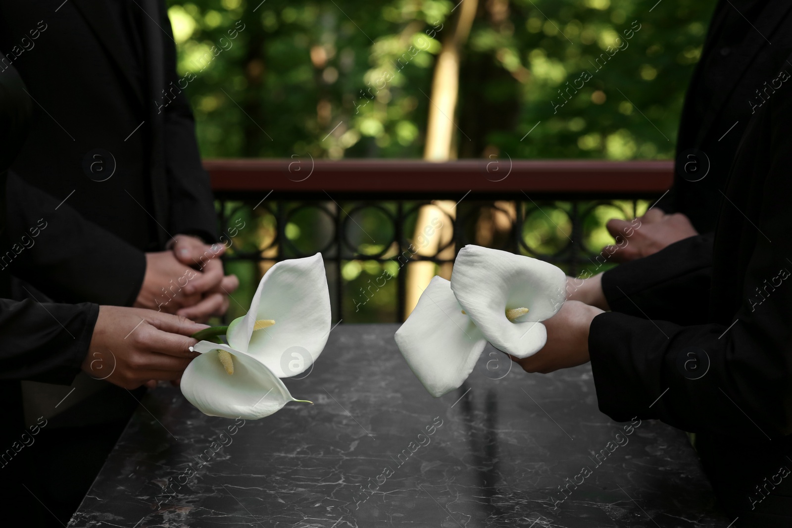 Photo of People with calla lily flowers near granite tombstone at cemetery outdoors, closeup. Funeral ceremony