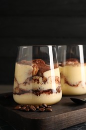 Photo of Delicious tiramisu in glasses and coffee beans on wooden board