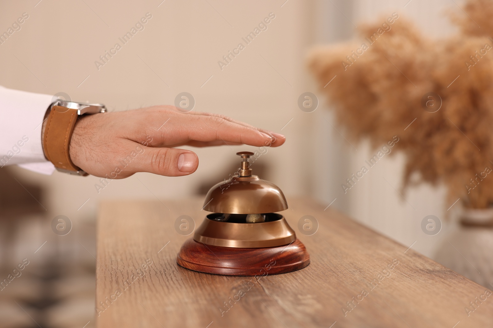 Photo of Man ringing service bell at wooden reception desk in hotel, closeup