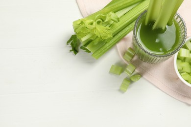 Photo of Glass of celery juice and fresh vegetables on white table, above view. Space for text