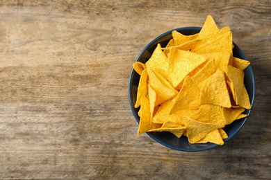 Photo of Tasty mexican nachos chips in color bowl on wooden table, top view. Space for text