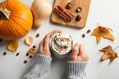 Woman holding cup with tasty pumpkin spice latte at light table, top view