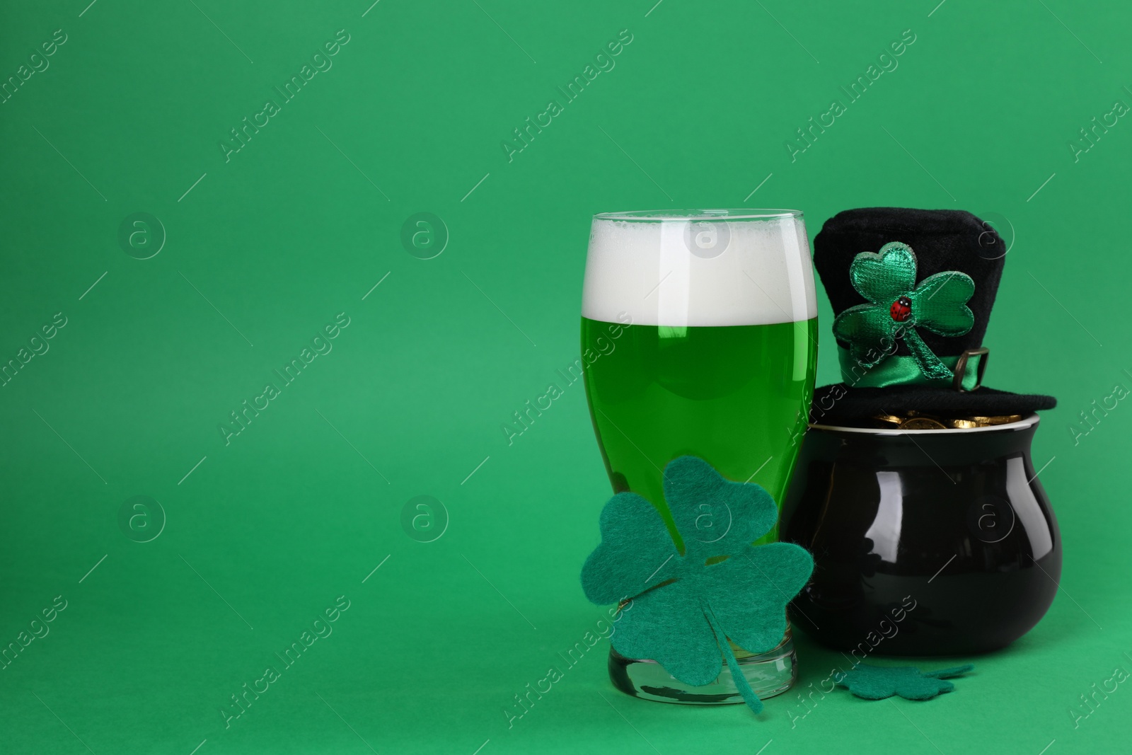 Photo of St. Patrick's day party. Green beer, leprechaun hat, pot of gold and decorative clover leaves on green background. Space for text
