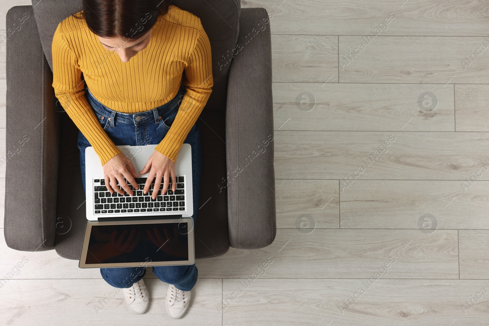 Photo of Woman working with laptop in armchair, top view. Space for text