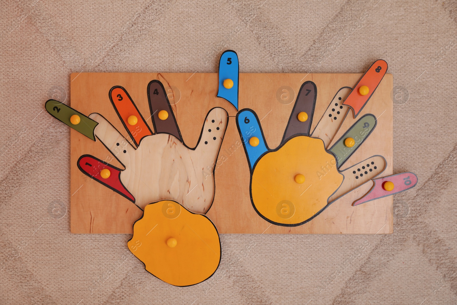 Photo of Wooden hands shaped puzzle on beige carpet, top view. Montessori toy