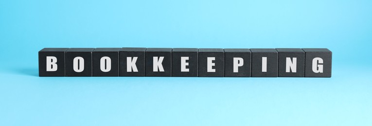 Photo of Word Bookkeeping made with black cubes on light blue background