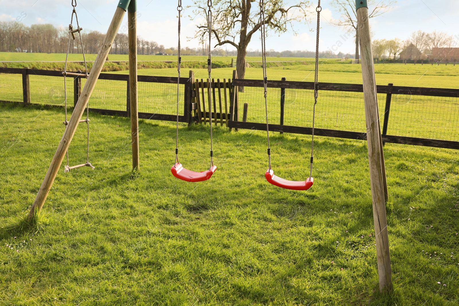 Photo of Outdoor swings on green grass near wooden fence outdoors