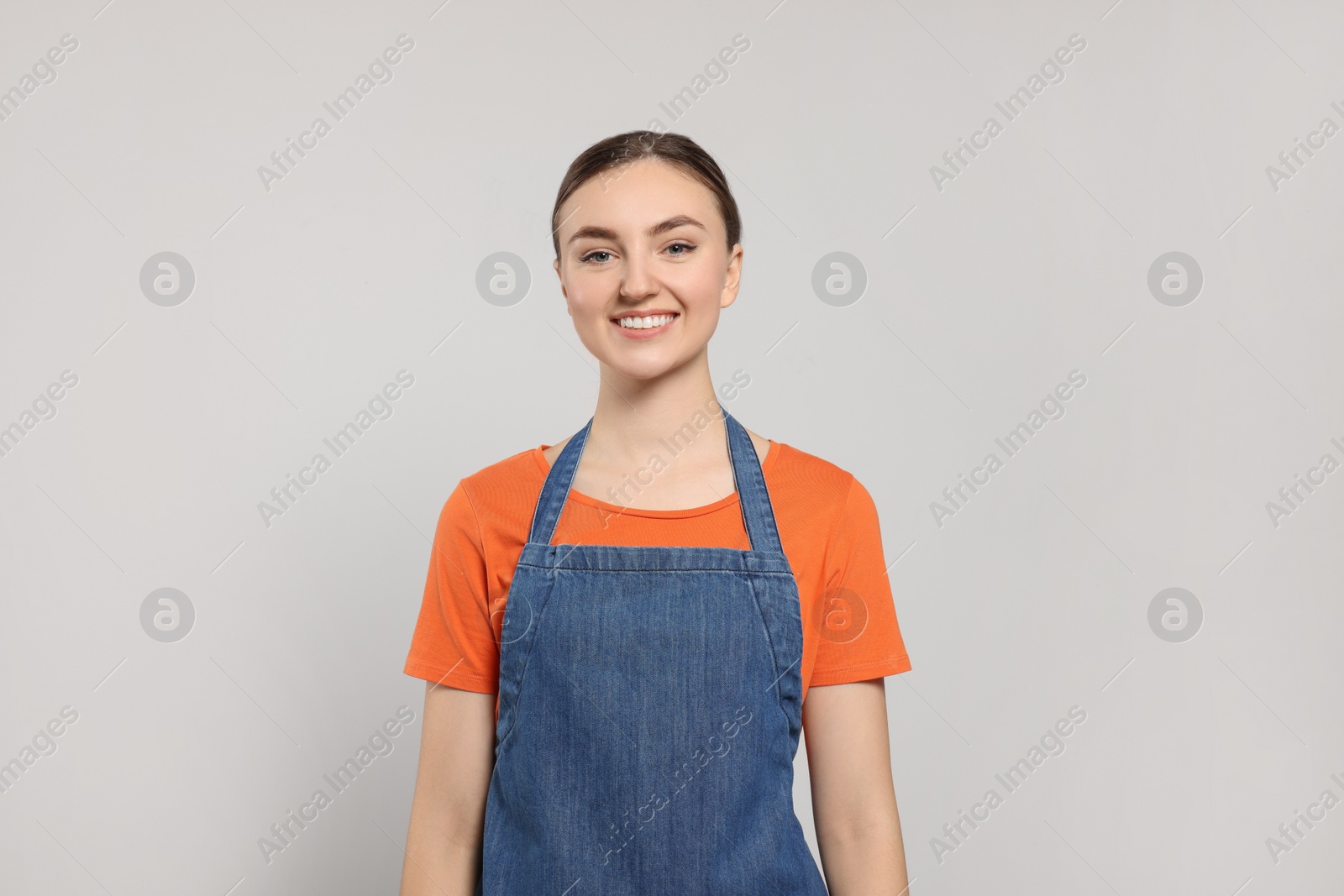 Photo of Beautiful young woman in clean denim apron on light grey background
