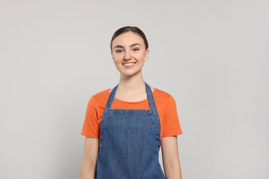 Beautiful young woman in clean denim apron on light grey background