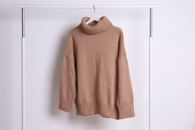 Warm sweater hanging on rack against white background