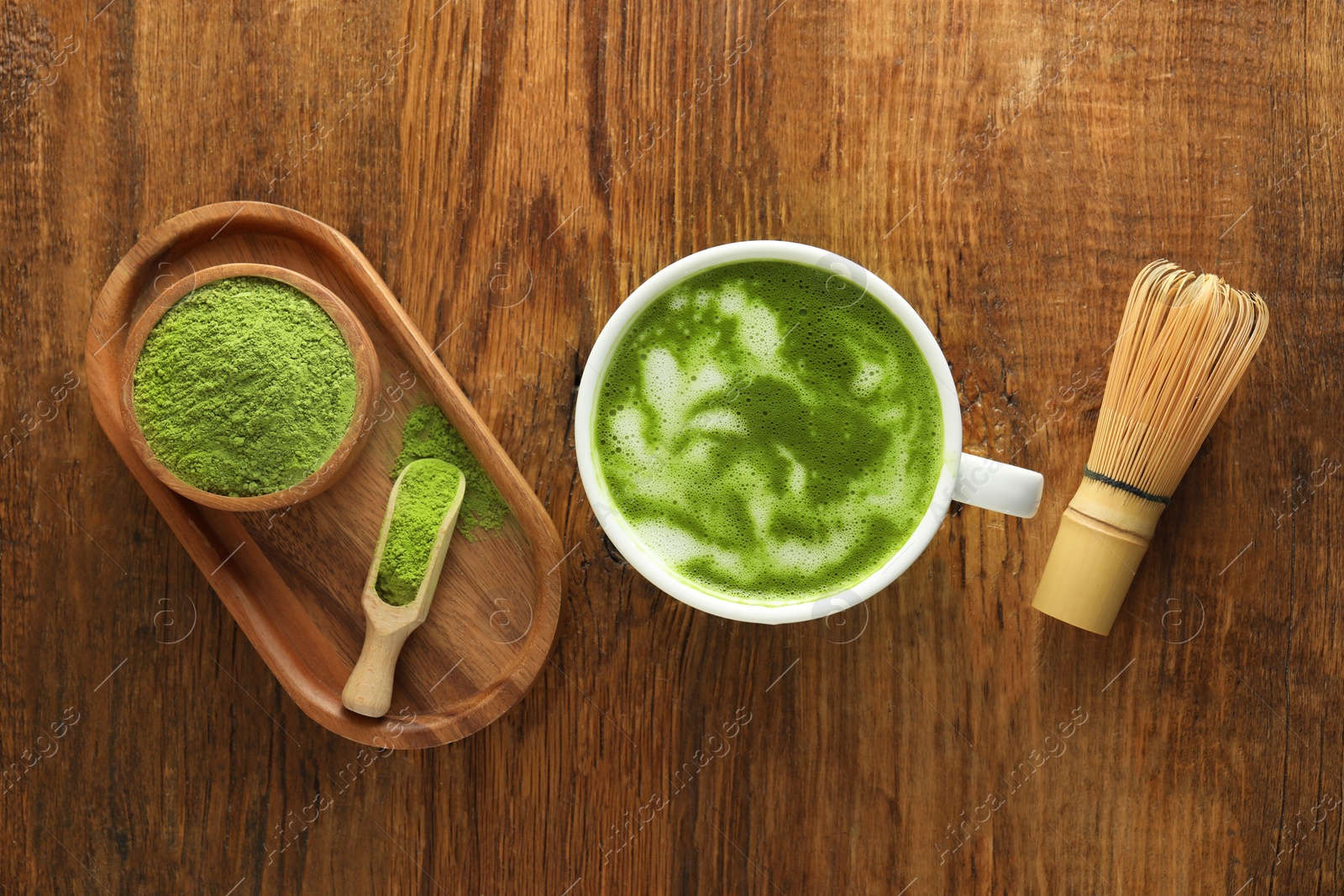 Photo of Cup of fresh matcha latte, powder and bamboo whisk on wooden table, flat lay