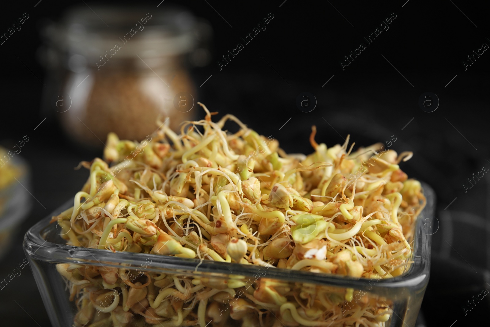 Photo of Glass bowl of sprouted green buckwheat on dark wooden table, closeup