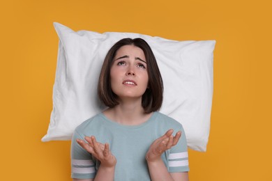 Photo of Unhappy young woman with pillow on yellow background. Insomnia problem
