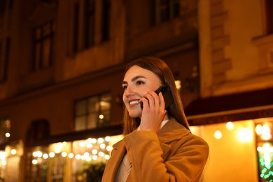 Smiling woman talking by smartphone on night city street