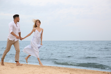 Happy couple running on beach, space for text. Romantic walk