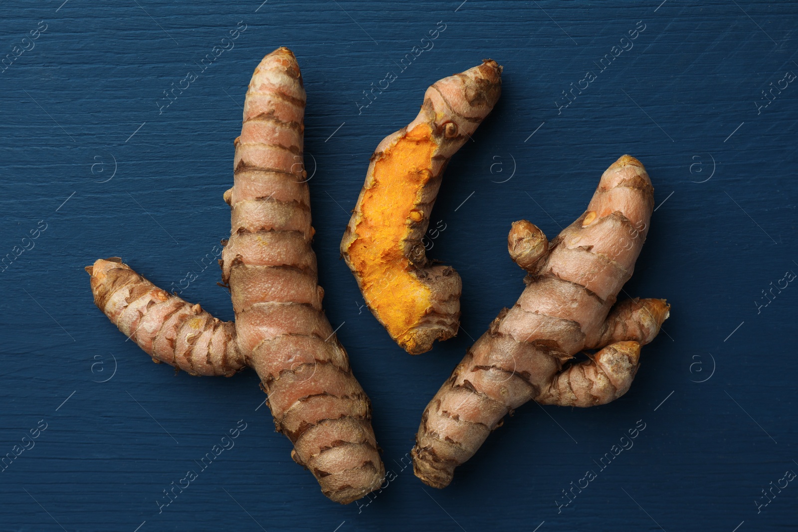Photo of Raw turmeric roots on blue wooden table, flat lay
