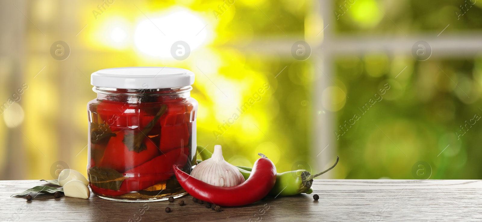 Image of Jar of tasty pickled chili peppers on wooden table in kitchen, space for text. Banner design 