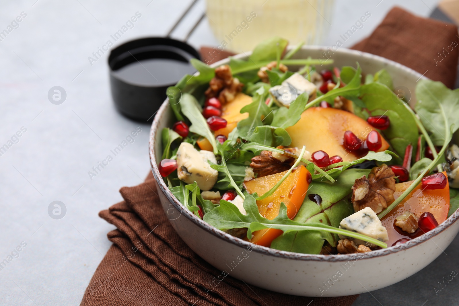 Photo of Tasty salad with persimmon, blue cheese, pomegranate and walnuts served on light grey table, closeup. Space for text