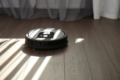 Modern robotic vacuum cleaner on wooden floor. Space for text