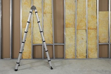 Photo of Ladder near wall with metal studs and insulation material indoors