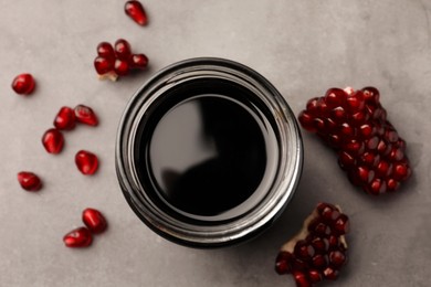 Glass jar of tasty pomegranate sauce and fresh ripe fruit on light grey table, flat lay