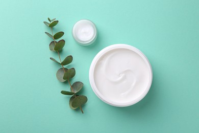 Moisturizing cream in open jars and eucalyptus branch on turquoise background, flat lay. Body care products