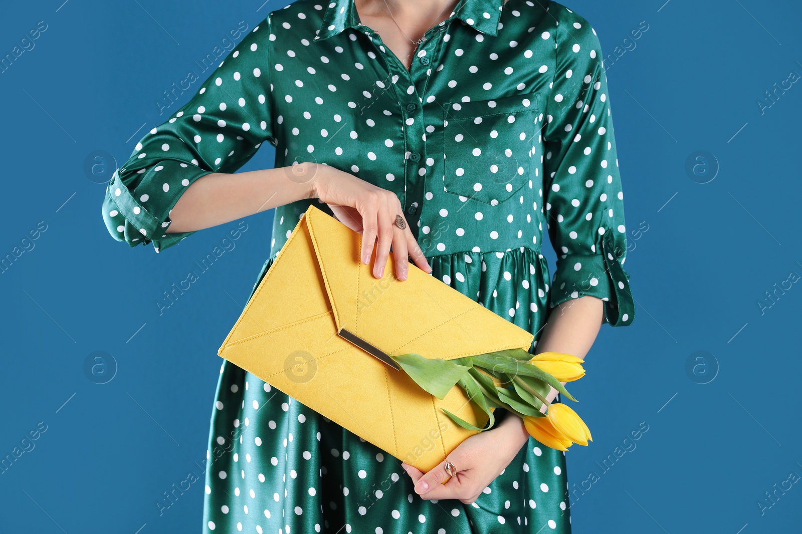 Photo of Woman holding elegant clutch with spring flowers on blue background, closeup