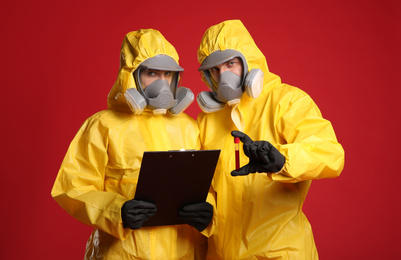 Photo of People in chemical protective suits with blood sample and clipboard on red background. Virus research