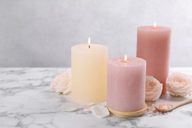 Spa composition with burning candles, flowers and sea salt on white marble table, space for text