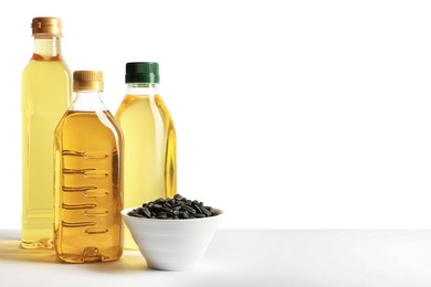 Photo of Bottles of different cooking oils and sunflower seeds on white background, space for text