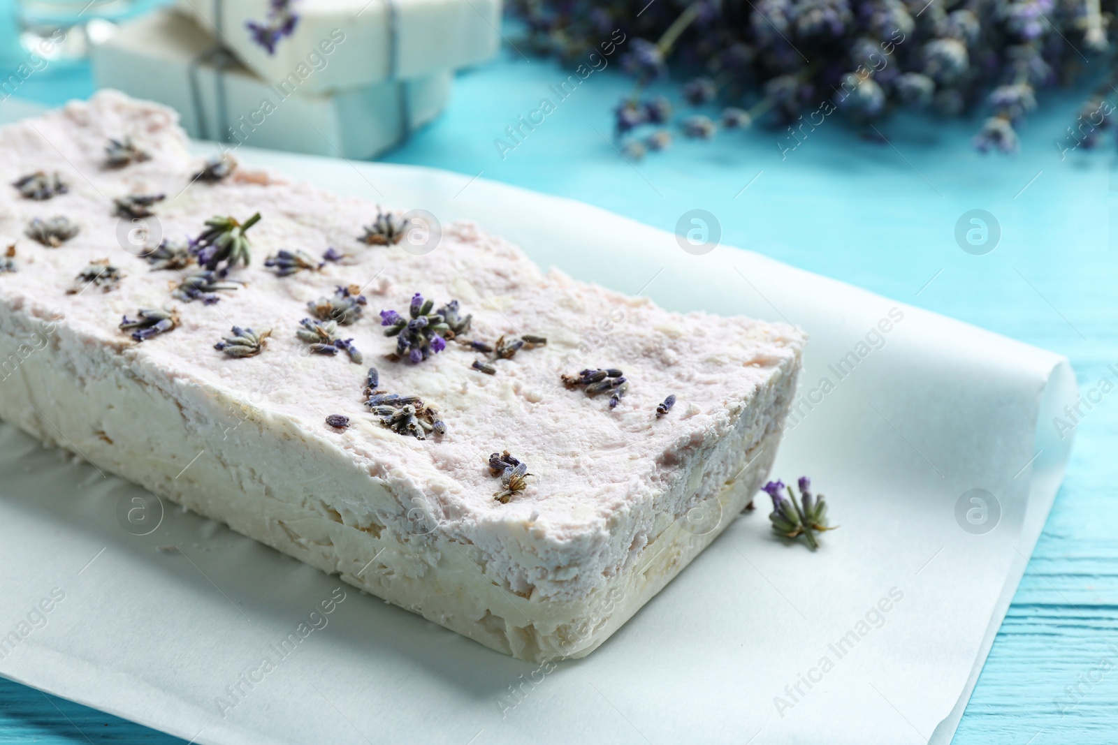 Photo of Hand made soap bar with lavender flowers on light blue wooden table, closeup